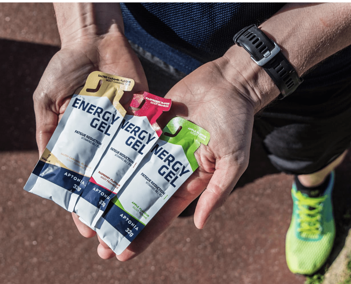 Persona sosteniendo tres sobres de gel energético Aptonia en diferentes sabores, ideal para deportistas.