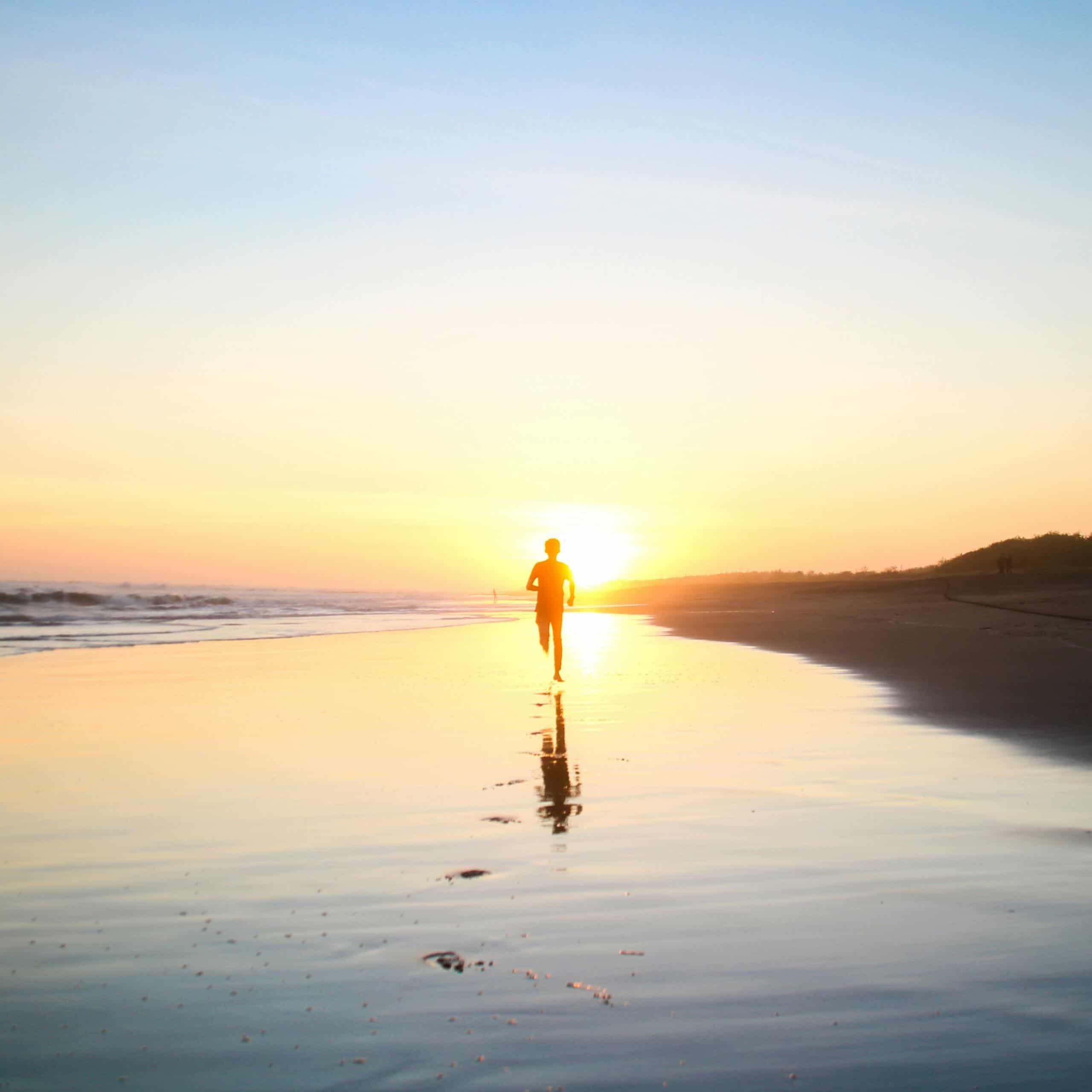 Silueta de una persona corriendo al amanecer en la playa, disfrutando cada paso de su rutina matutina.